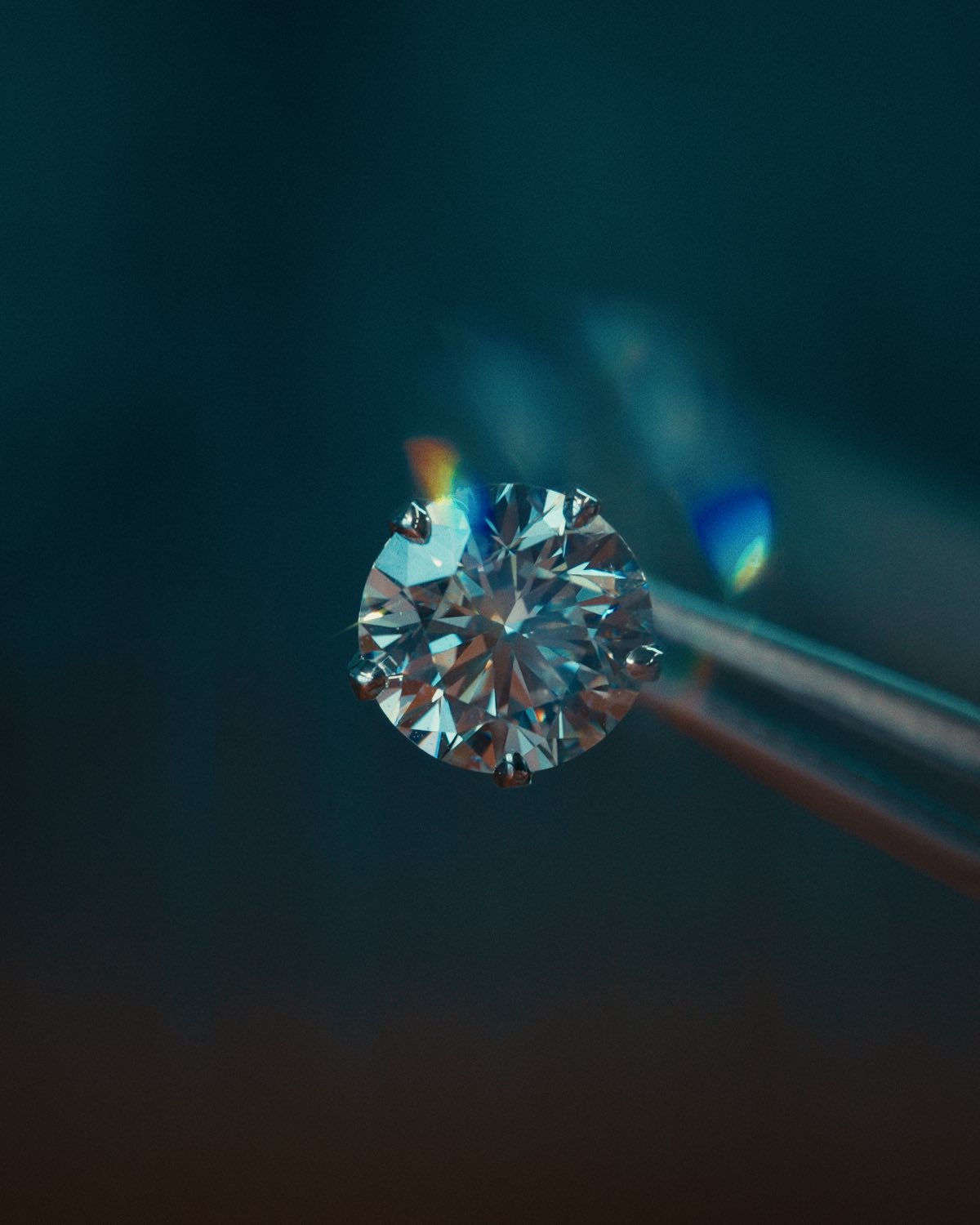 A diamond held in tweezers against a deep blue dark