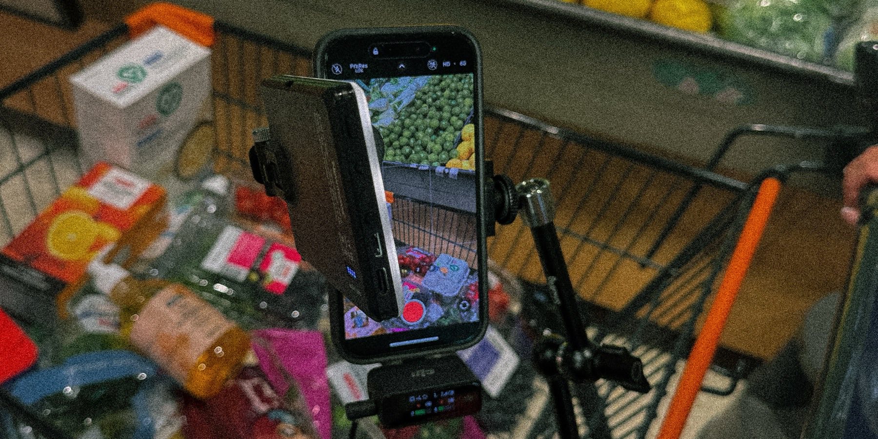 A phone clamped to a shopping trolley, recording the aisle, with the groceries in frame on its screen